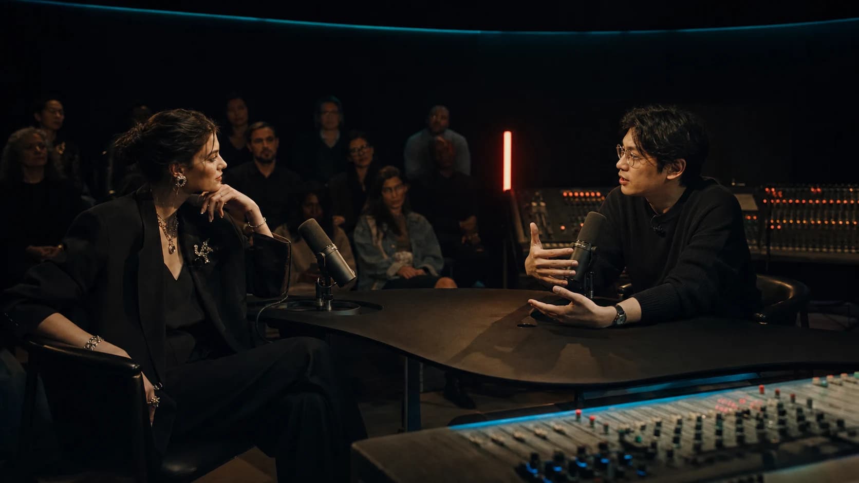 A fictional cultural interviewer and AI founder in an intimate broadcast studio